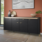 A modern black sideboard cabinet with gold-tone handles and legs, styled in a room with a terracotta wall, decorative vases, and a framed abstract print.