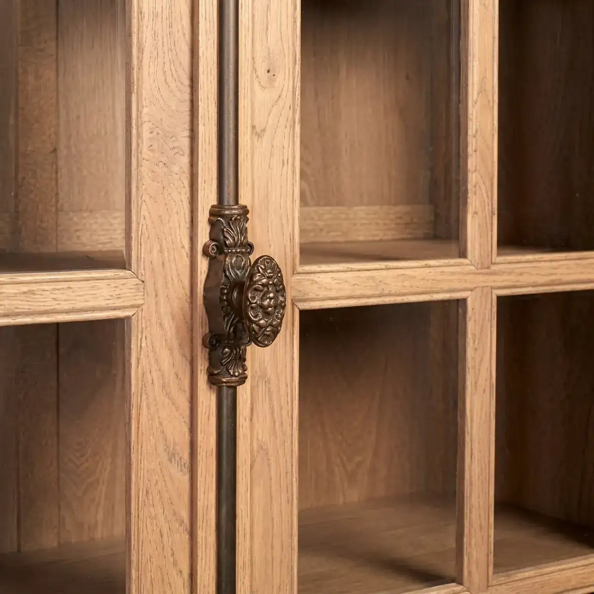 Close-up of a wooden cabinet door with a dark bronze ornate pull handle and matching vertical bar, showing warm wood grain and glass panes.