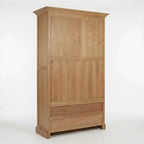 A tall wooden wardrobe or armoire with a natural oak finish, featuring two upper doors and a lower drawer, shown against a plain white studio background.