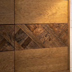 A mid-century modern wooden sideboard with six drawers, featuring a herringbone wood inlay pattern across the center. 