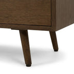 Close-up of a mid-century modern wooden cabinet or sideboard, showing the dark brown wood grain, drawer front, and tapered legs on a white background.
