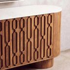 A close-up of a modern wooden sideboard or cabinet with a curved white marble top and carved vertical oval patterns on the front, set against a neutral textured wall.