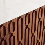 Close-up of a modern wooden cabinet with a white marble countertop, featuring a carved geometric pattern of interlocking vertical ovals.