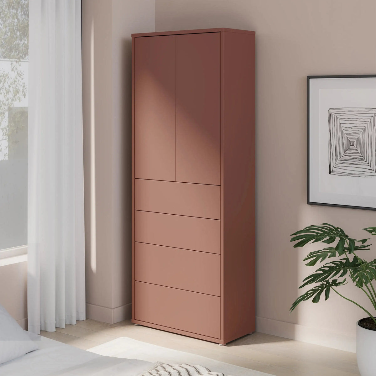 Tall pink wardrobe in a bedroom with a plant and framed picture on the wall.