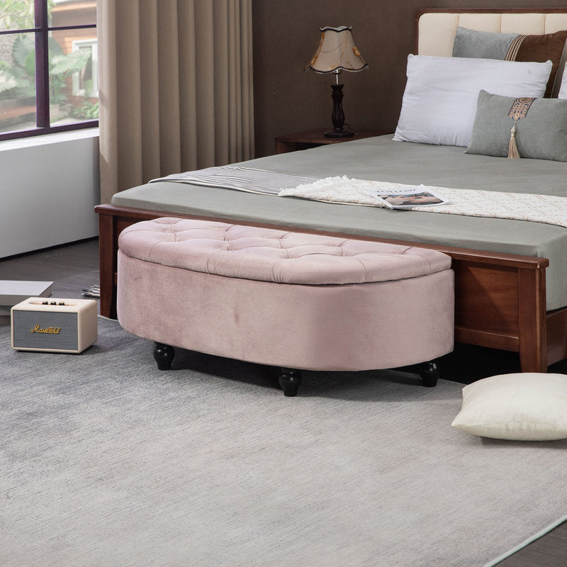 Round beige ottoman in front of a bed in a bedroom setting.