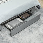 Gray bed with open drawer revealing folded blankets and pillows on a light gray floor.