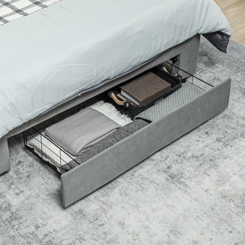 Gray bed with open drawer revealing folded blankets and pillows on a light gray floor.