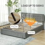 Gray upholstered bed with steel legs and wood slats, featuring a plant and curtains in the background.