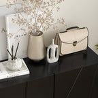 Beige handbag on a black surface with decorative items including a vase and books.