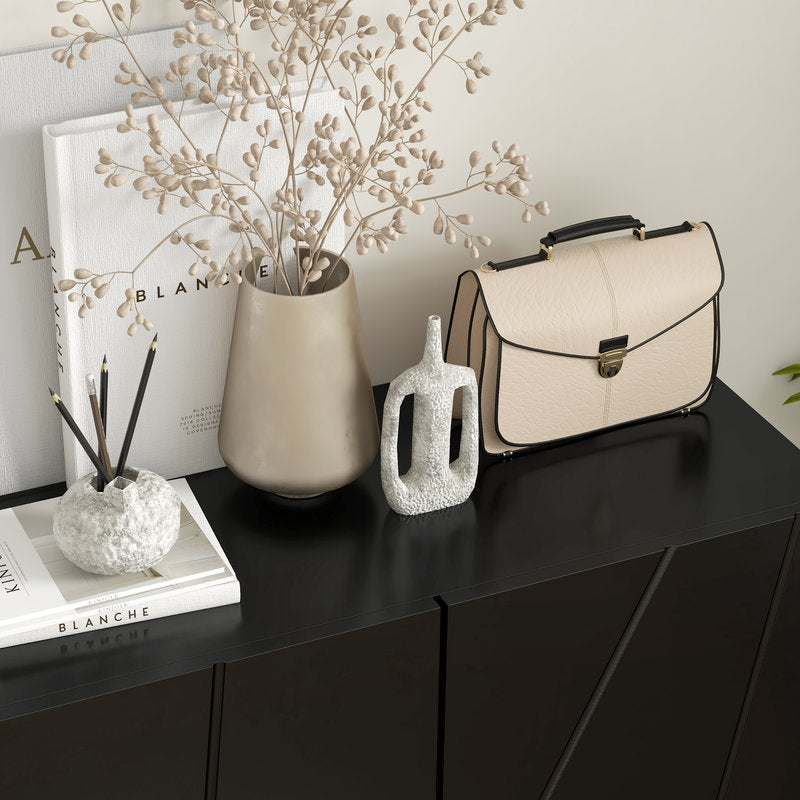 Beige handbag on a black surface with decorative items including a vase and books.