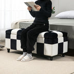 Person sitting on a checkered ottoman reading a book in a bedroom.