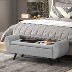 Gray upholstered bench in front of a bed with decorative items on top