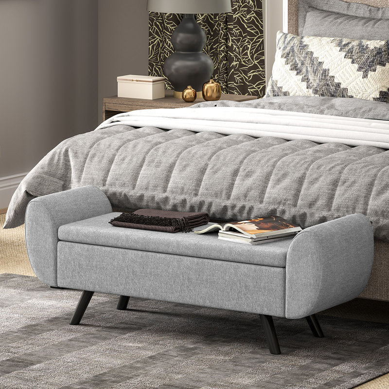 Gray upholstered bench in front of a bed with decorative items on top