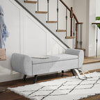 Gray upholstered bench in a home setting with a staircase and rug.