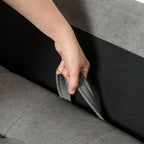 Person adjusting a gray fabric panel on a sofa.