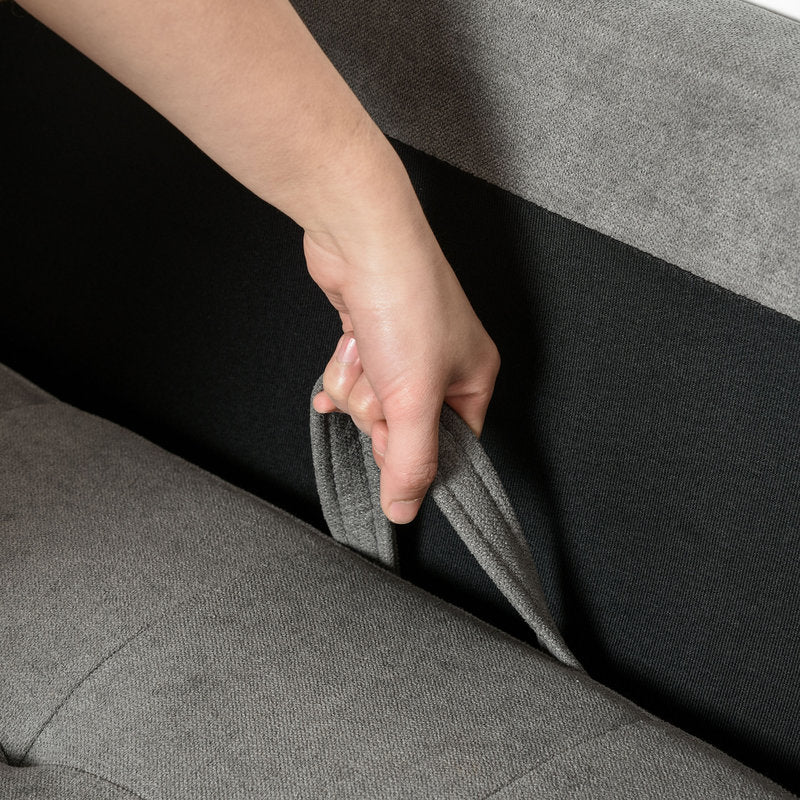 Person adjusting a gray fabric panel on a sofa.