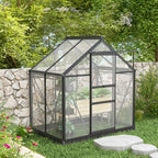 Small greenhouse in a garden setting with greenery and a stone wall.