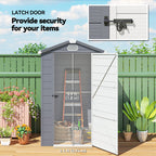 Outdoor storage shed with a latch door, plants, and a green fence.