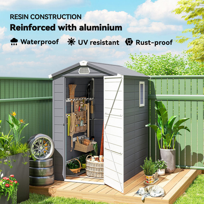 Resin storage shed with open door, showing tools and plants, against a green fence and blue sky.