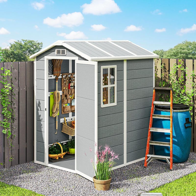 Grey garden shed with tools and items, surrounded by greenery and a blue rain barrel.