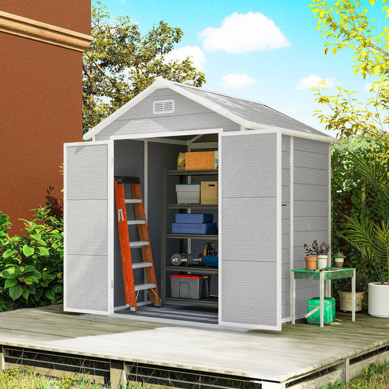 Gray storage shed with open doors on a wooden deck, surrounded by greenery.
