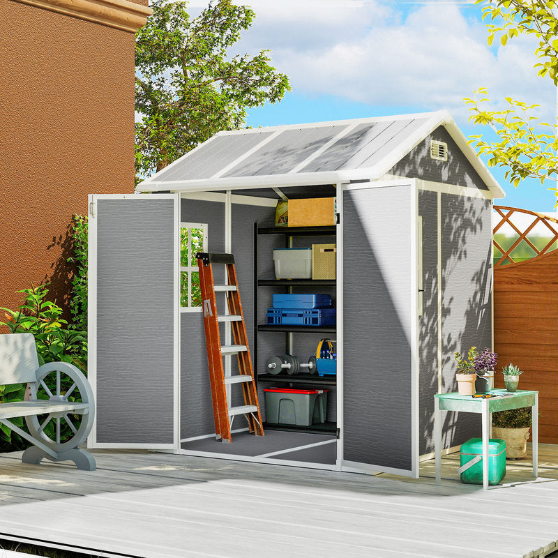 Gray storage shed with open doors on a wooden deck, surrounded by greenery and a clear sky.