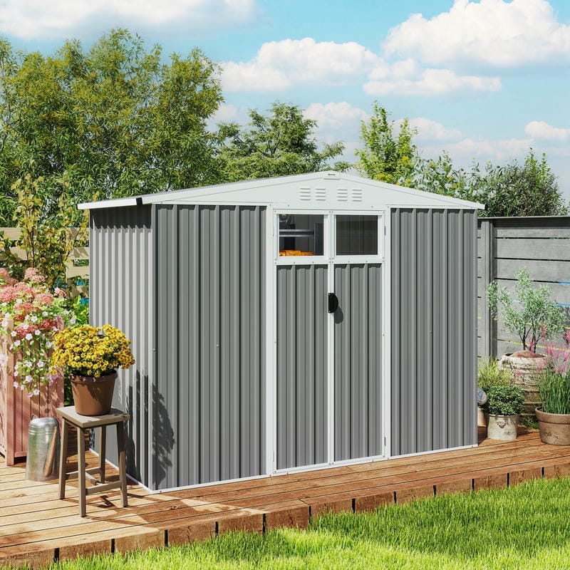 Light grey galvanised steel garden shed on a wooden deck surrounded by plants and flowers