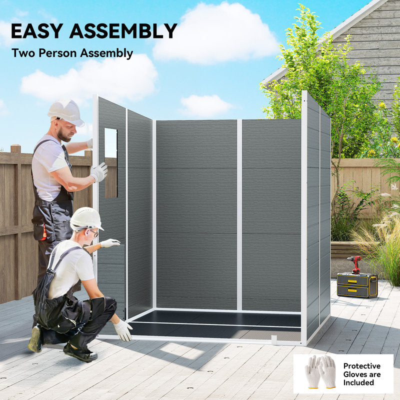Two people assembling a gray outdoor privacy screen with tools and protective gloves on a wooden deck.