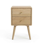A light natural oak two-drawer nightstand with tapered legs and small round brass knobs, shown on a white background.